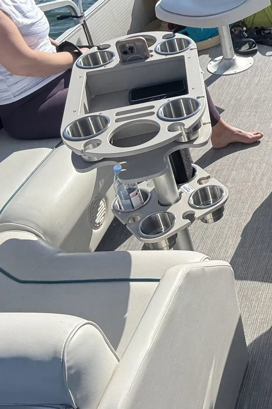 A light gray aluminum dual-position boat table with integrated cup holders and a phone holder, shown on a boat with a person seated nearby.