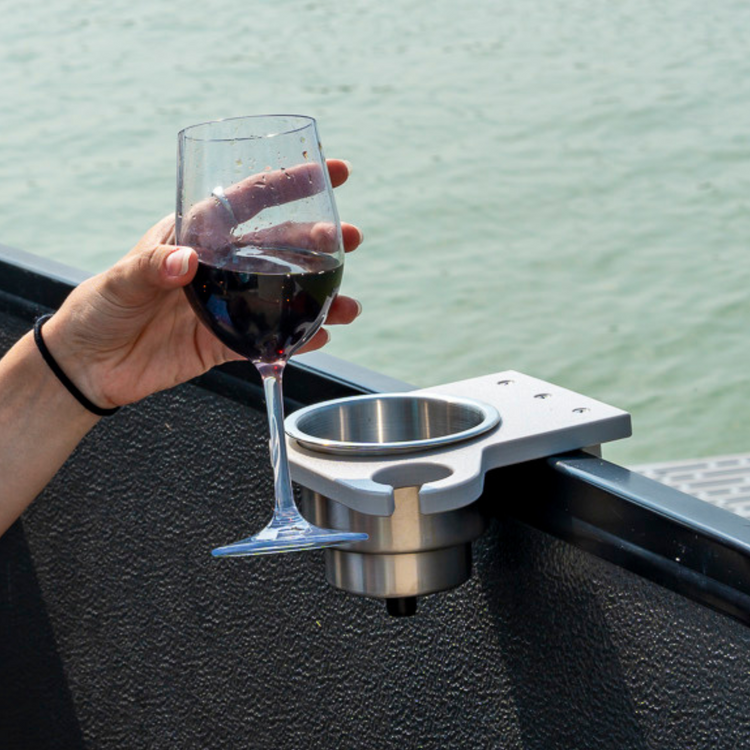 Hand holding a glass of red wine over a boat's cup holder with water in the background