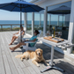 Two women sitting on a deck with a dog, enjoying a meal outdoors.