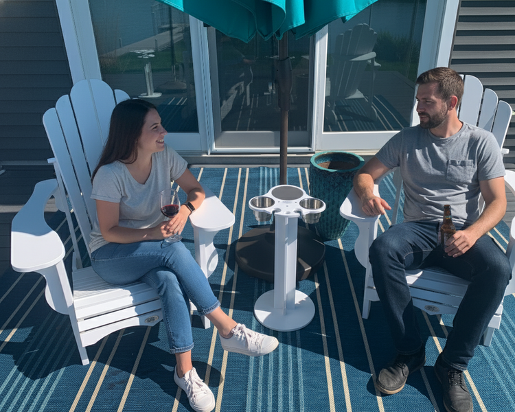 Two people sitting on Adirondack chairs under a teal umbrella on a patio.