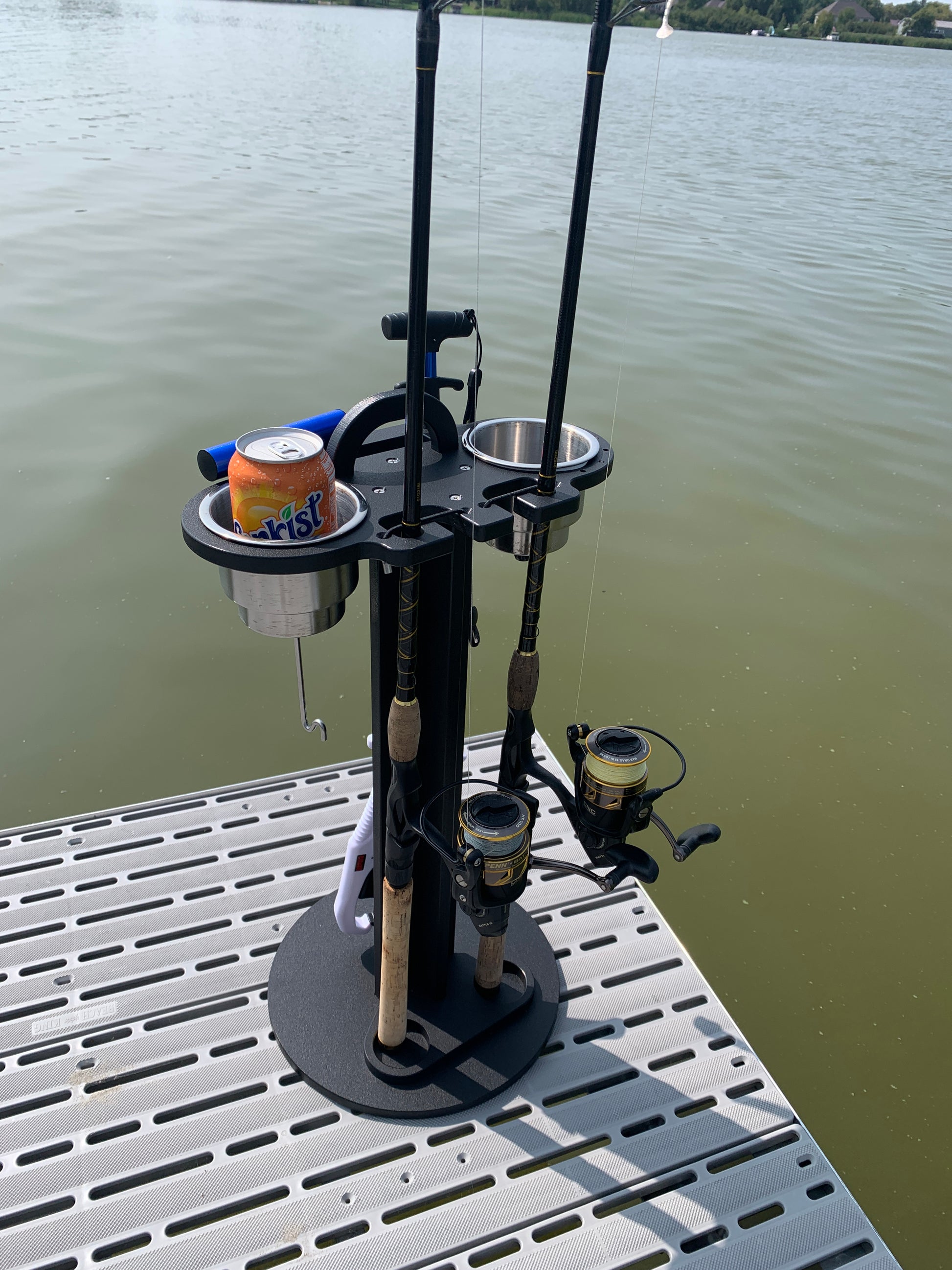 Soda can in a 2 pc cup holder, fishing rod holder caddy near a water body.