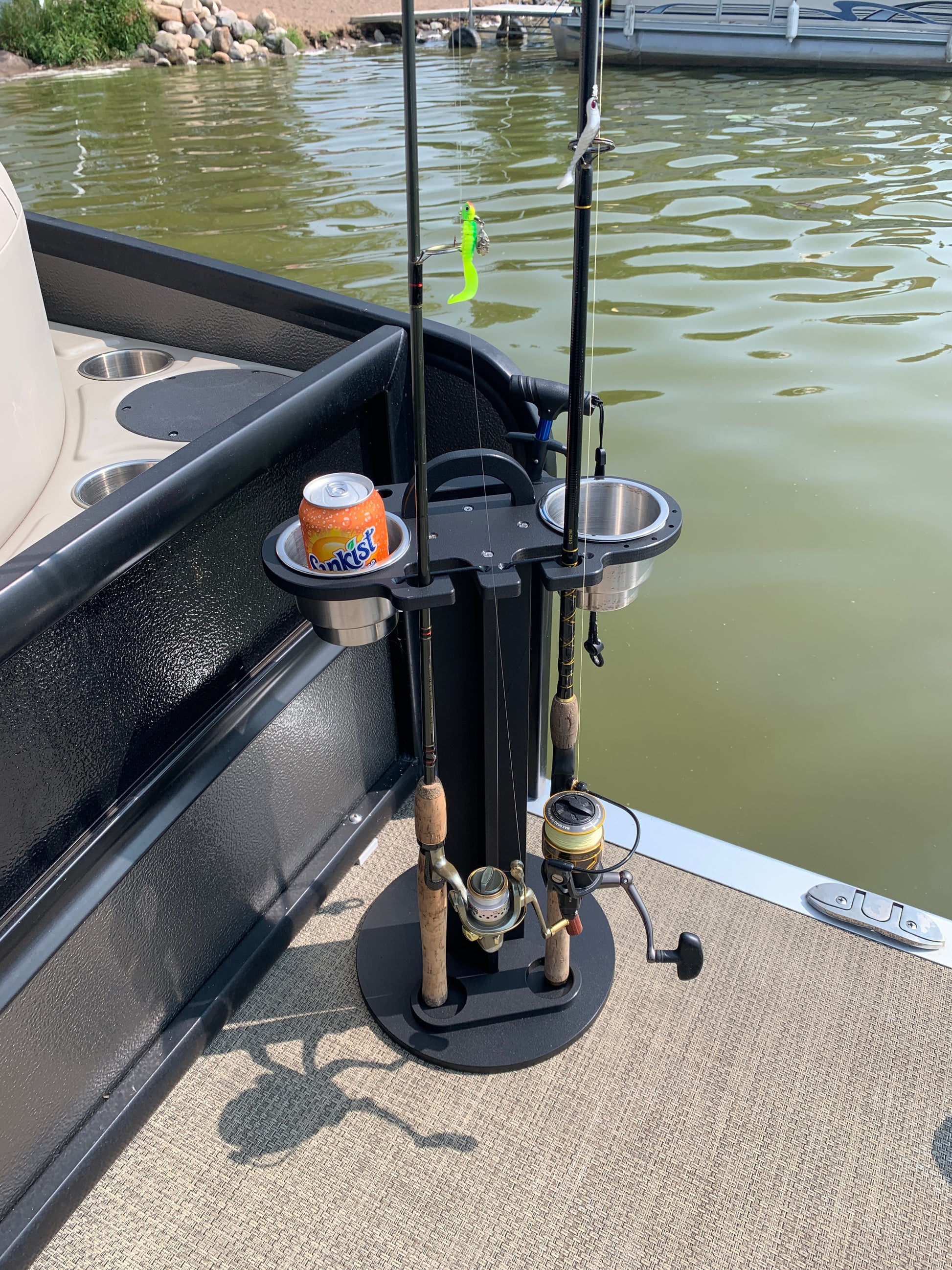 Soda can in a 2 pc cup holder, fishing rod holder caddy near a water body.
