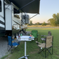 Outdoor setup with RV, table, and chairs in a grassy area.