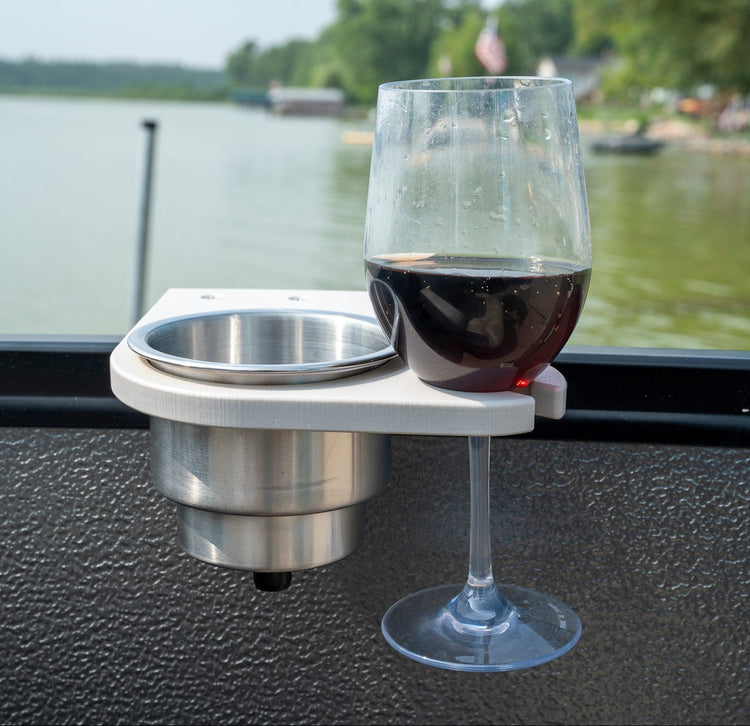 A stainless steel and white marine wine glass holder mounted on a boat's textured deck, holding a glass of red wine with a scenic lake background.